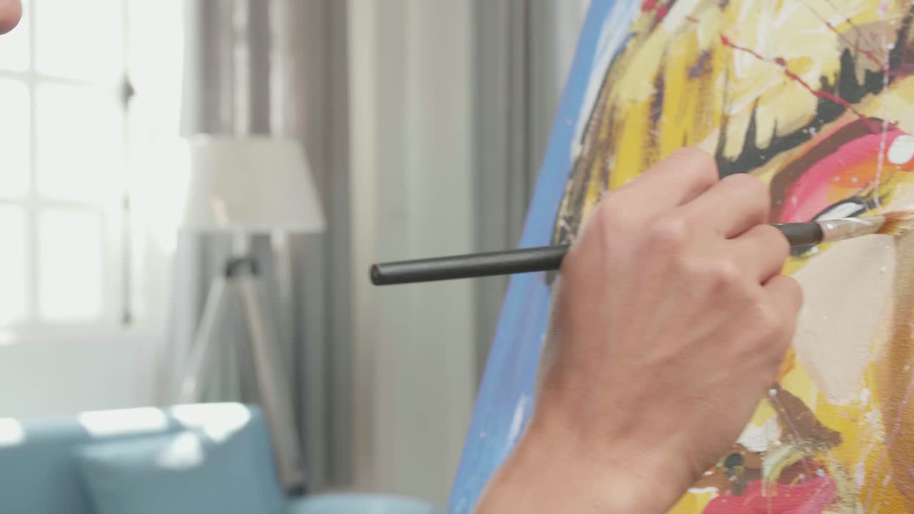 vista lateral cercana de un artista asiático hombre sosteniendo un pincel de colores mixtos y pensando antes de pintar la cara de una chica en el lienzo