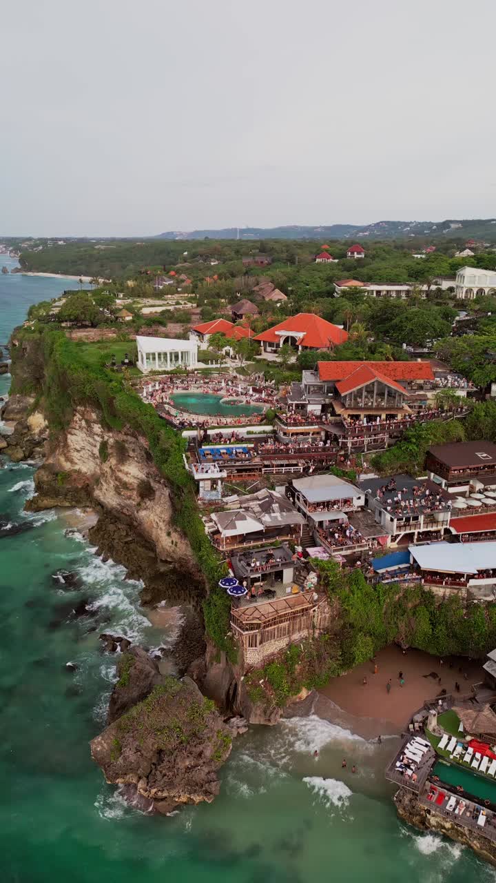 Stunning vertical footage captures Uluwatu Beach by Blue Point Resort in Bali, with a pool perched on a cliff, a hidden cave below, and people enjoying a breathtaking sunset view