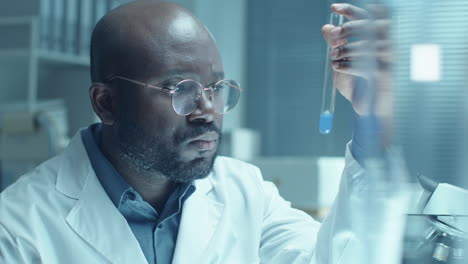 black male scientist examining blue liquid in test tube in laboratory