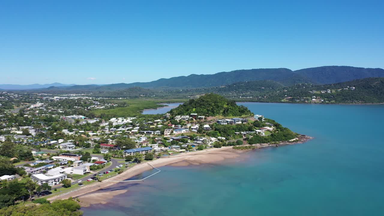 Lenta panoramica con drone intorno all'area edificata di Airlie Beach, Queensland - case sulla montagna con un lungo tratto di spiaggia in primo piano, giornata di sole limpida