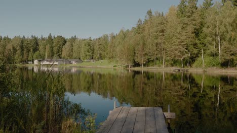 pov walking to wooden bridge at kypesjön lake with open-air yard in background, borås, sweden - wide shot tracking forward and truning left