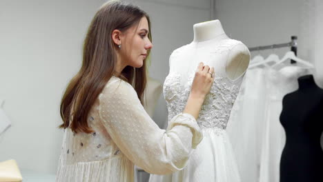 Portrait-of-a-girl-creating-a-wedding-dress-by-exclusive-order-sewing-fabrics-and-rhinestones-on-a-dress-dressed-in-a-mannequin.-production-of-wedding-dresses.-Little-business