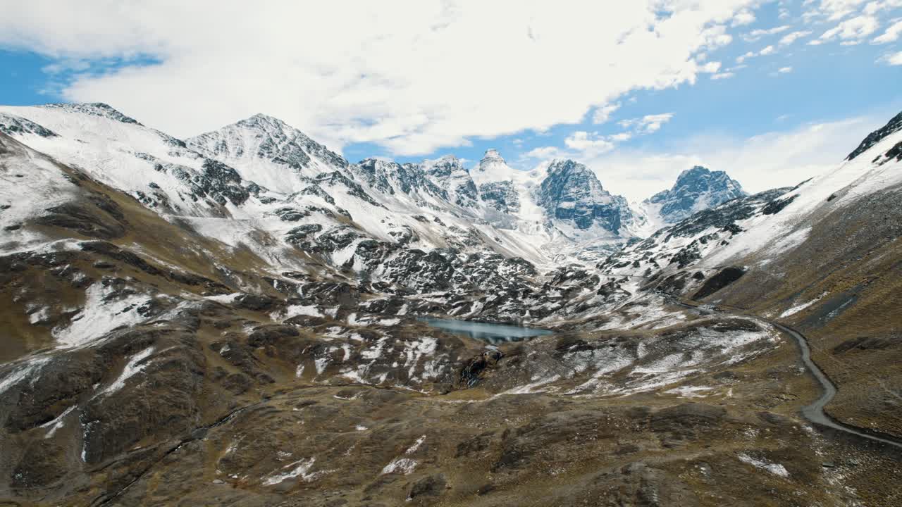 Filmato aereo mozzafiato con drone delle aspre montagne andine innevate del Pico Austria. Un remoto lago glaciale è incastonato tra le cime sotto un cielo blu limpido nell'Altopiano boliviano