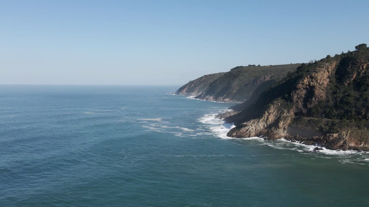 Costa selvaggia del Sudafrica con montagne verdi e onde oceaniche che si infrangono sulle rocce.