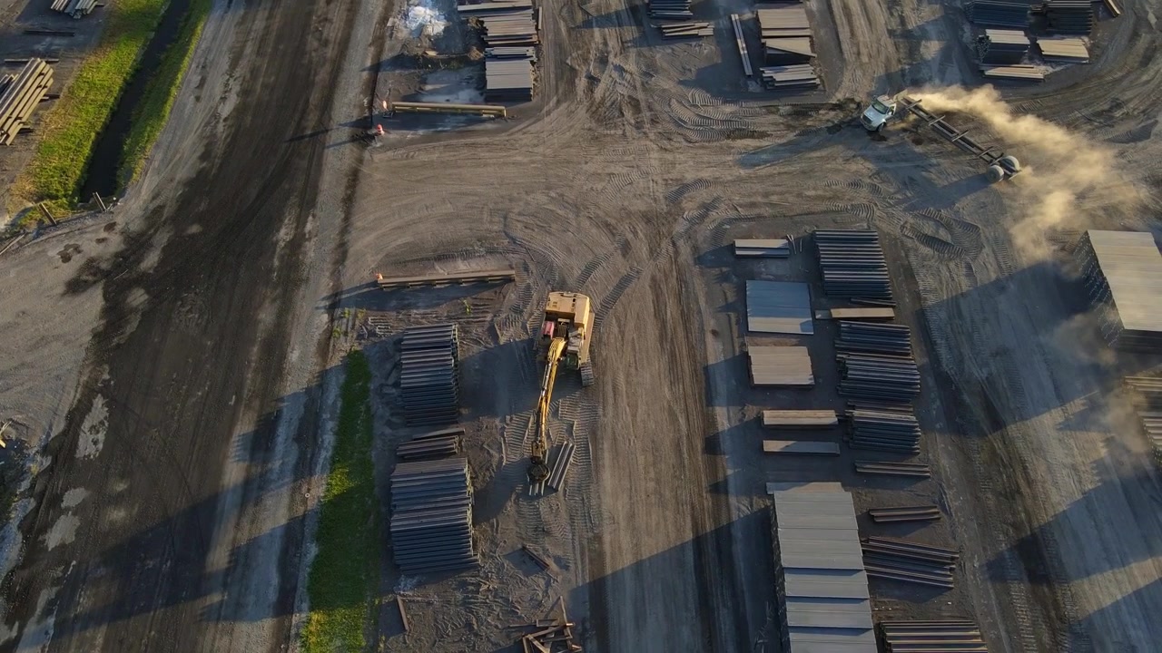 Magnet equipped tracked loader stacks metal I-beams. Aerial orbit with drone. 4K 29.97fps