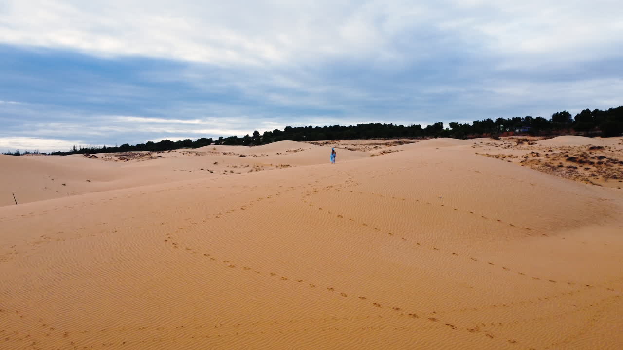 매력적인 젊은 여성은 파란색 드레스를 입고 붉은 모래 언덕에서 햇빛을 즐기고 공중에서 시야를 향해 날아갑니다