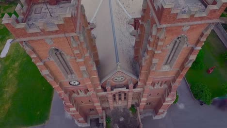 a beautiful old church top close up aerial view, red building of the church, green trees and grass around the church, cross at the top and bottom of the church