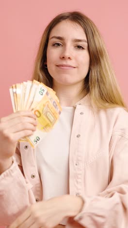 young woman holding and counting euro banknotes on pink background