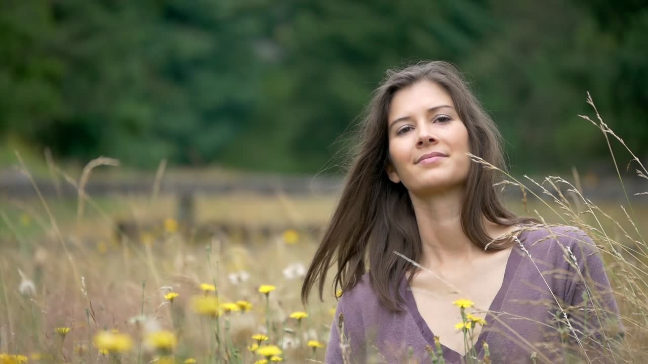 Incredible slow motion elegant hair flip by beautiful young woman while relaxing in a field of gorgeous flowers looking at camera