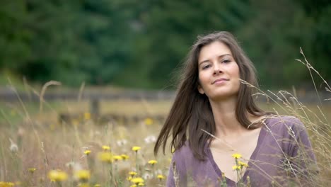 incredible slow motion elegant hair flip by beautiful young woman while relaxing in a field of gorgeous flowers looking at camera