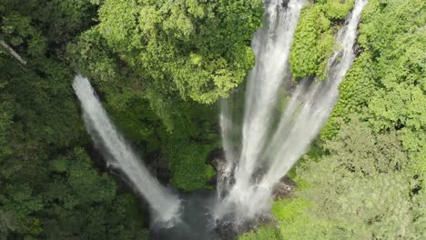 Descending-drone-of-lush-jungle-waterfall-with-water-mist-in-sunlight