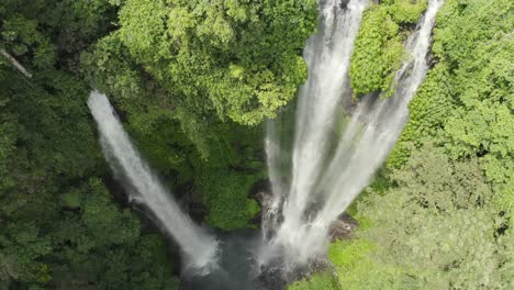 descending drone of lush jungle waterfall with water mist in sunlight