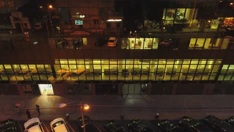 4k outside view of business district building , mall with wall mirror windows at evening or night .  reflection of city , people , cars in mirrored walls . drone camera moving . people working inside
