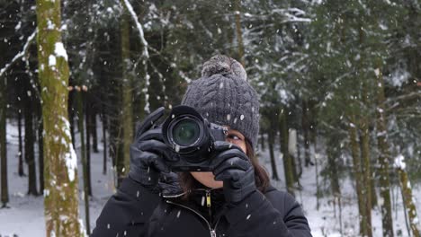Attractive-woman-taking-pictures-of-winter-forest-during-snowfall,-static-view