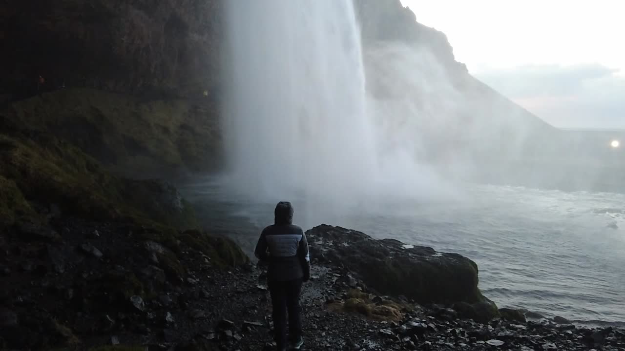 niña de pie y mirando hacia la cascada en cámara lenta de cueva en islandia