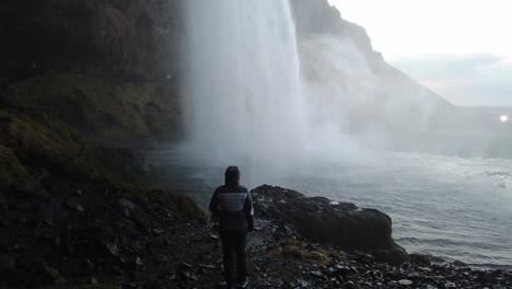 girl standing and looking up at waterfall in cave slowmotion in iceland