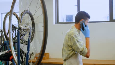 Man-talking-on-mobile-phone-while-repairing-bicycle-4k