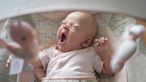 yawning baby girl in child rocker with toys