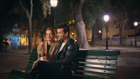 Romantic people flirting evening date eating strawberry in urban park together.