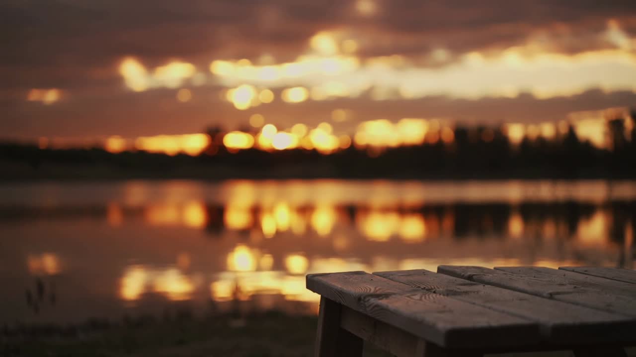 Indramning af en træbænk, der fanger skiftende glimt, mens solen sænker sig bag trærækken over søen, med plads til tekst