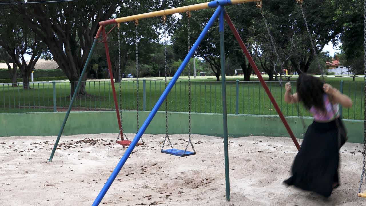 mujer joven con falda larga y camisa colorida balanceándose y riéndose sintiéndose libre y feliz en un parque visto desde el frente con cámara fija con movimiento de cámara deslizante