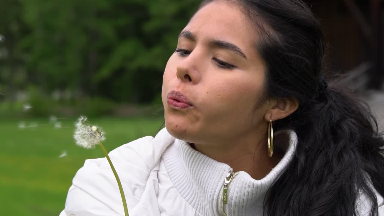 Happy Latina woman blowing dandelion in green park, close up view