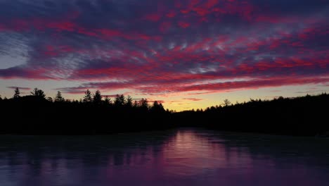 aerial slide over a frozen pond with the forest silhouetted against a colorful sunrise