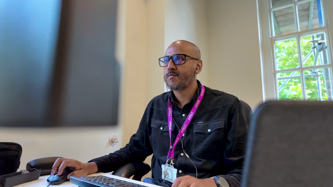 un hombre trabaja con entusiasmo en un entorno de oficina, sentado frente a pantallas y usando un teclado, encarnando el concepto de dedicación y productividad
