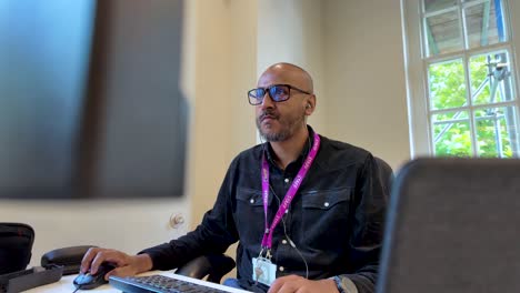 un hombre trabaja con entusiasmo en un entorno de oficina, sentado frente a pantallas y usando un teclado, encarnando el concepto de dedicación y productividad