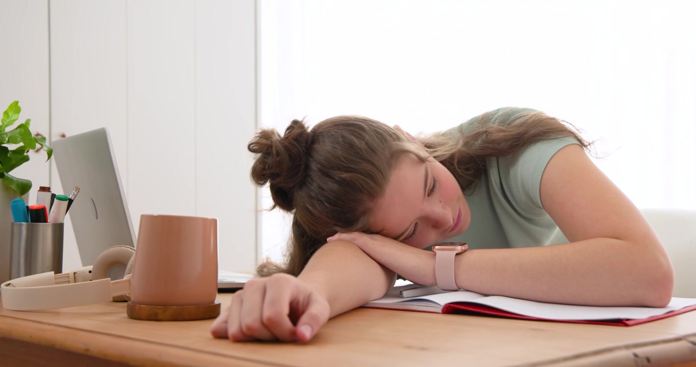 Donna che lavora al laptop e al quaderno alla scrivania di casa, stancandosi, strofinandosi gli occhi e appoggiando la testa.