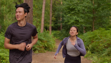 mid adult couple exercising doing work out outdoors running through forest with man encouraging tired woman wearing sports clothing 1