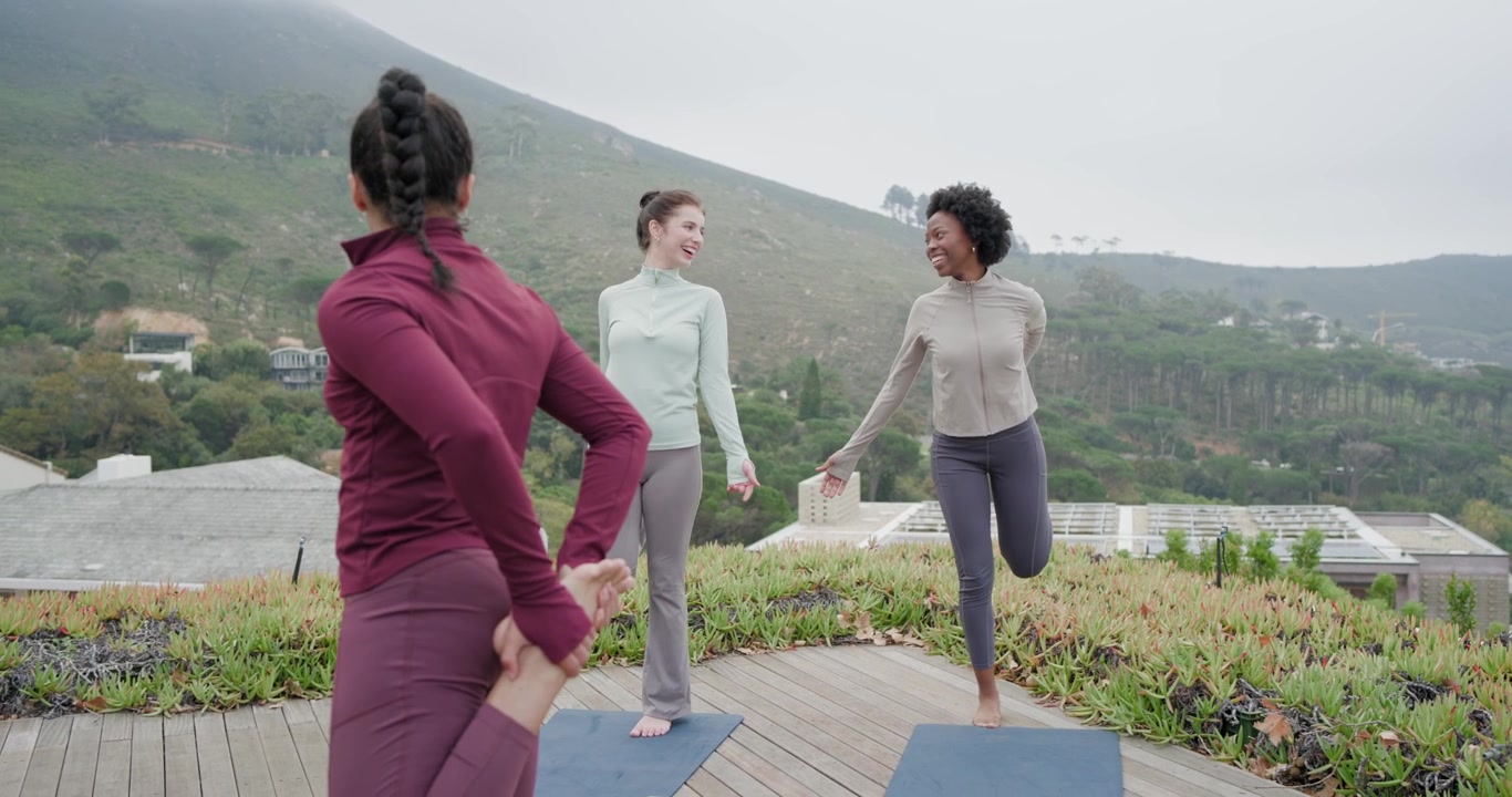 Donne di diverse etnie che seguono un istruttore, facendo un passo avanti ed eseguendo uno stretching per i quadricipiti per l'equilibrio su tappetini sul tetto.
