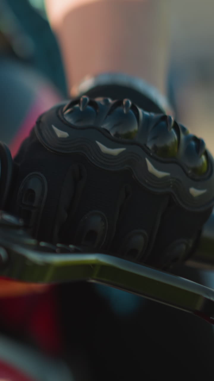 Close-up of a biker s hand gripping the clutch lever while wearing protective gloves on a motorcycle, with a blurred background of something fluttering in the wind and a red bike