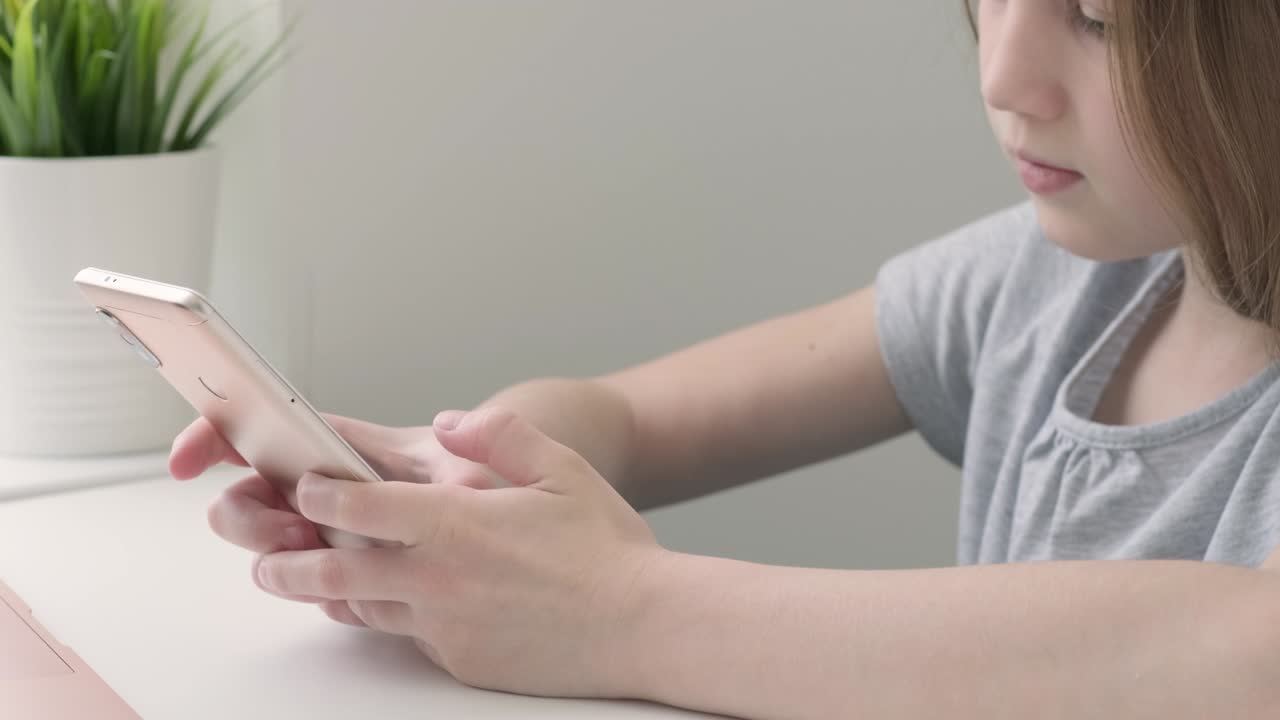 Kid girl using texting mobile phone or chat in home in the morning and sunlight, side view