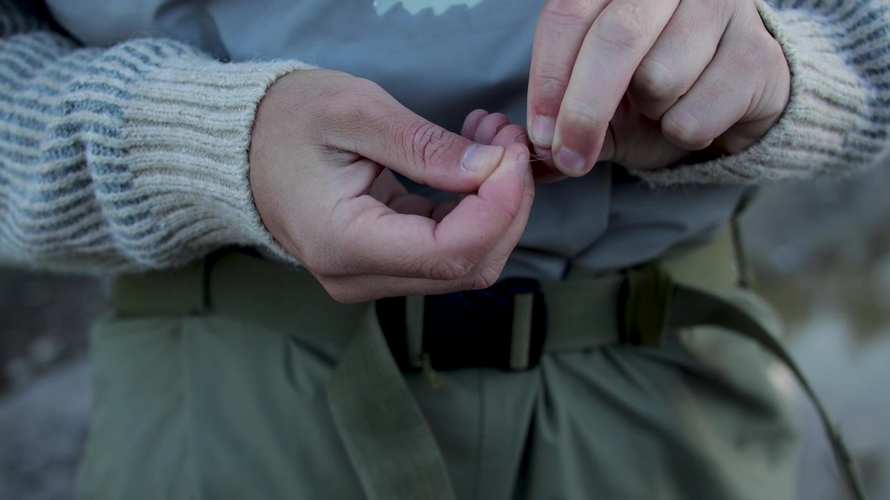 Rekaman darat close-up diam seorang nelayan mengikat umpan lalat baru ke joran pancing lalatnya di samping danau alpine yang tenang di Grand Mesa, Colorado, bersiap untuk menangkap ikan trout pelangi dan brook.