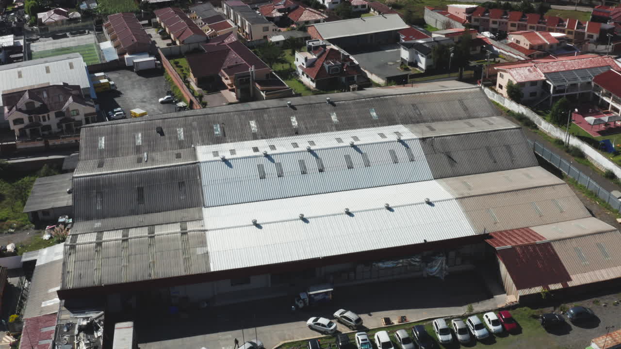 Aerial shot captured with a drone showing a landscape composed of homes, a factory, mountains in the background, and large green areas.