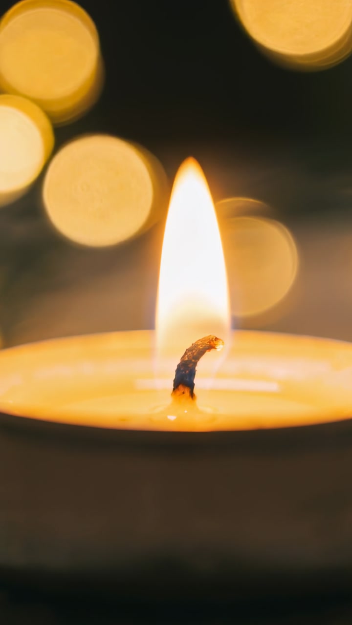 Vertical video: Tealight candle burning, flame heating wick and melting wax with bokeh for wellness