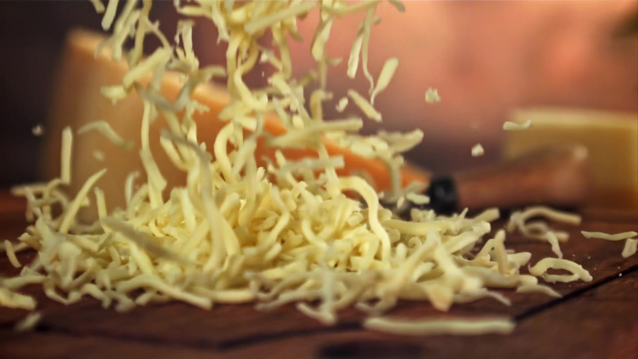 Grated cheese falling onto a wooden table in slow motion