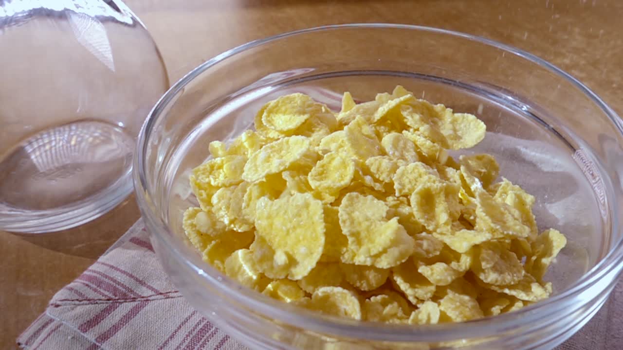 Fiocchi di mais gialli croccanti nella ciotola per una deliziosa colazione mattutina con latte. Slow motion con ripresa rotatoria.