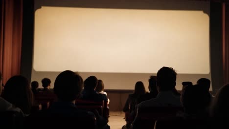 audience members watching a bright, empty screen in a dark movie theater create a captivating atmosphere of anticipation