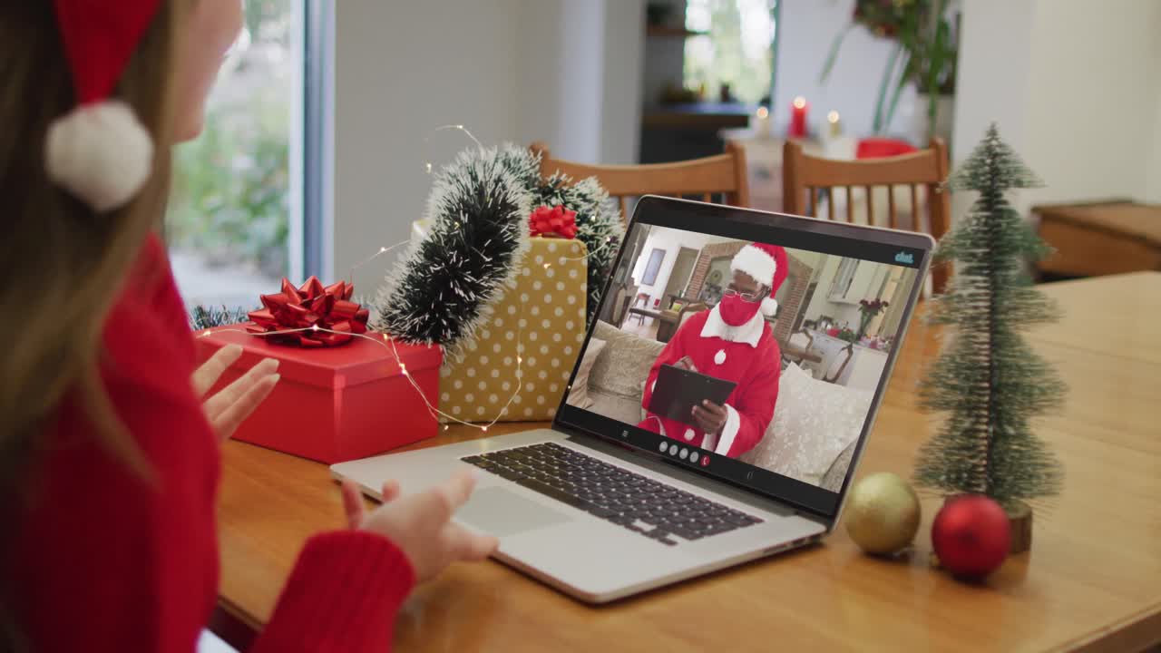mujer caucásica feliz en videollamada con santa claus con máscara facial en tiempo de navidad