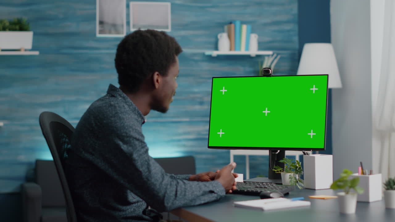 Wide shot of african american man talking on video call on computer with mock up chroma display