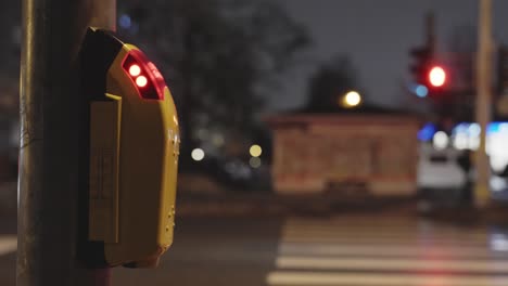 button at traffic lights on pedestrian crossing, city at night with a red light