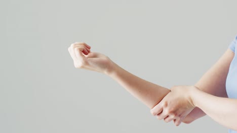 백인 여성의 중간 부분의 비디오가 복사 공간으로 회색 배경에 팔을 마사지하고 있습니다.
