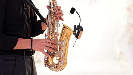 saxophonist in black shirt and trousers plays jazz on golden saxophone with microphone. musician male performs music on a saxophone against the blurred background. live performance.