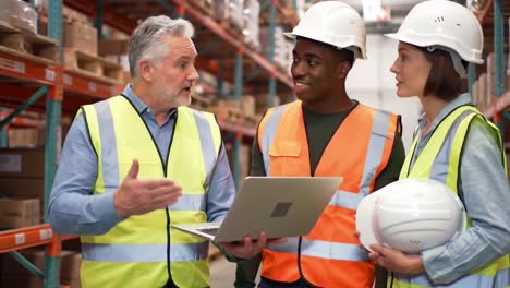 diverse warehouse management team, two men and a woman, use a laptop for planning and discussion