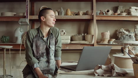 female potter video calling on laptop in workshop