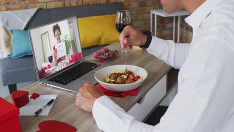 Diverse-couple-on-a-valentines-date-video-call-woman-on-laptop-screen-holding-marry-me-sign-man-eati
