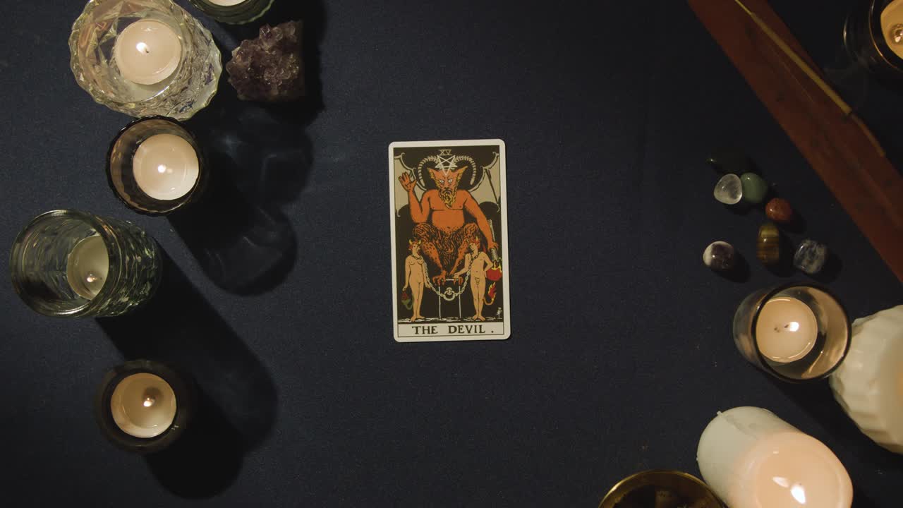 toma aérea de una persona que da una lectura de cartas del tarot que establece el diablo, el mundo y las cartas de las estrellas en la mesa