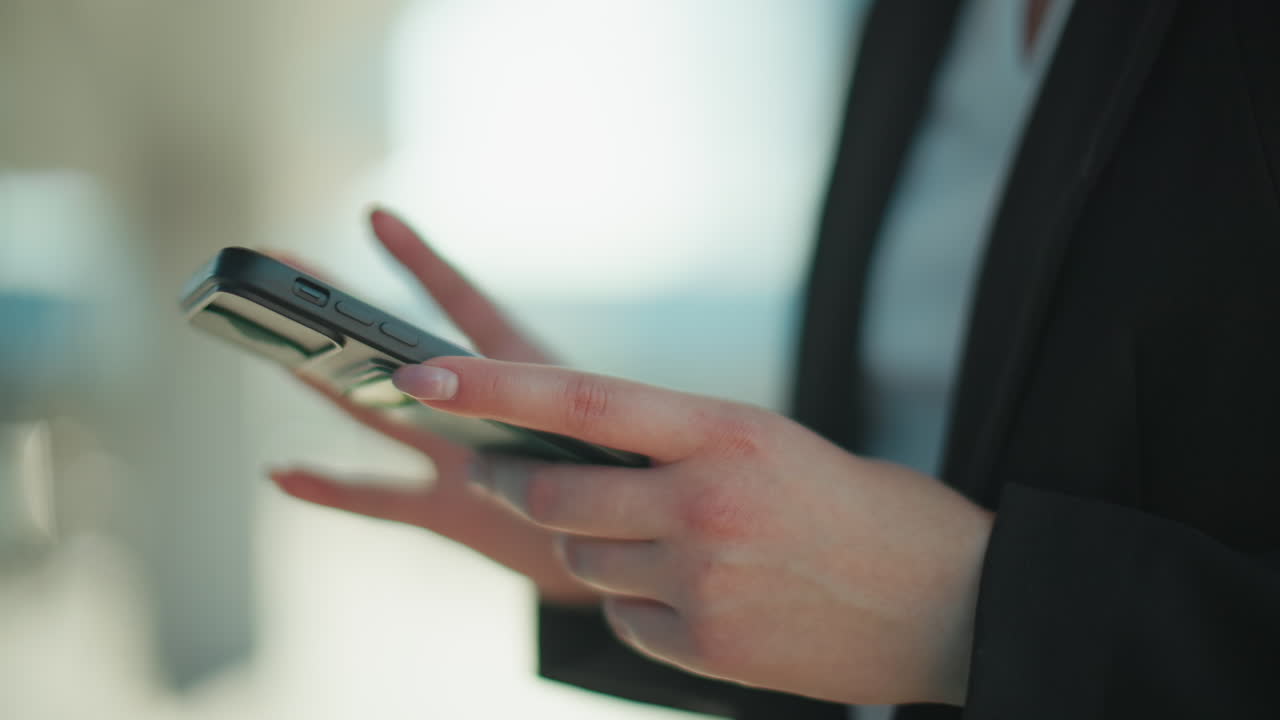 Primo piano di una donna che scorre lo schermo del telefono, digitando messaggi, con uno sfondo sfocato di un edificio in un contesto urbano, che mette in evidenza affari, produttività e comunicazione moderna